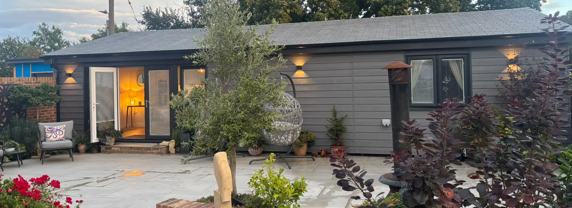 Two-bedroom granny annexe set in a landscaped garden with basket chairs on a paved patio area.